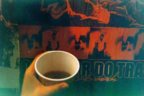 Foto analógica de uma mão segurando um copo de café diante de um mural vermelho e verde